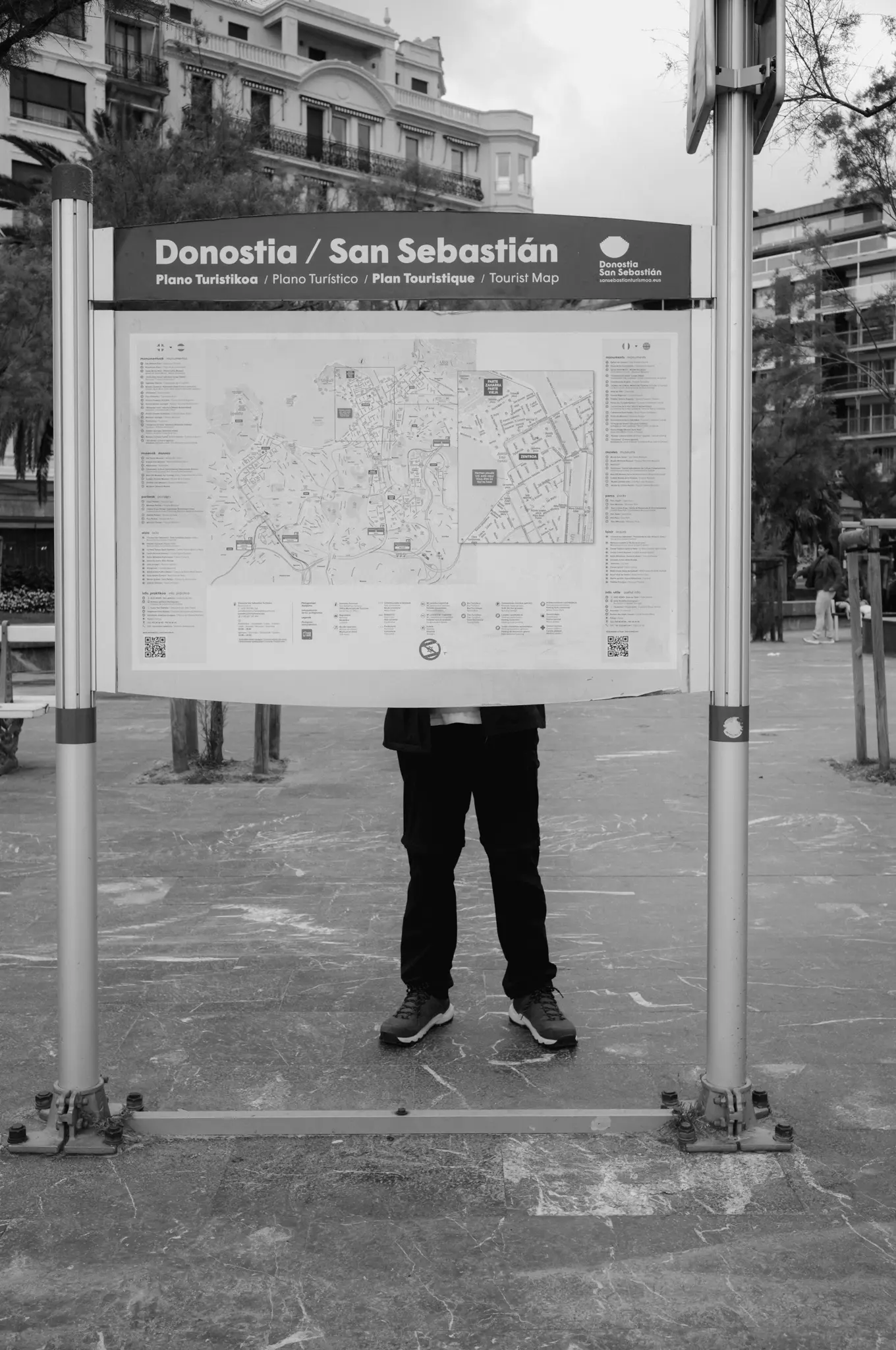 A person standing behind a tourist map board, only their legs showing beneath it