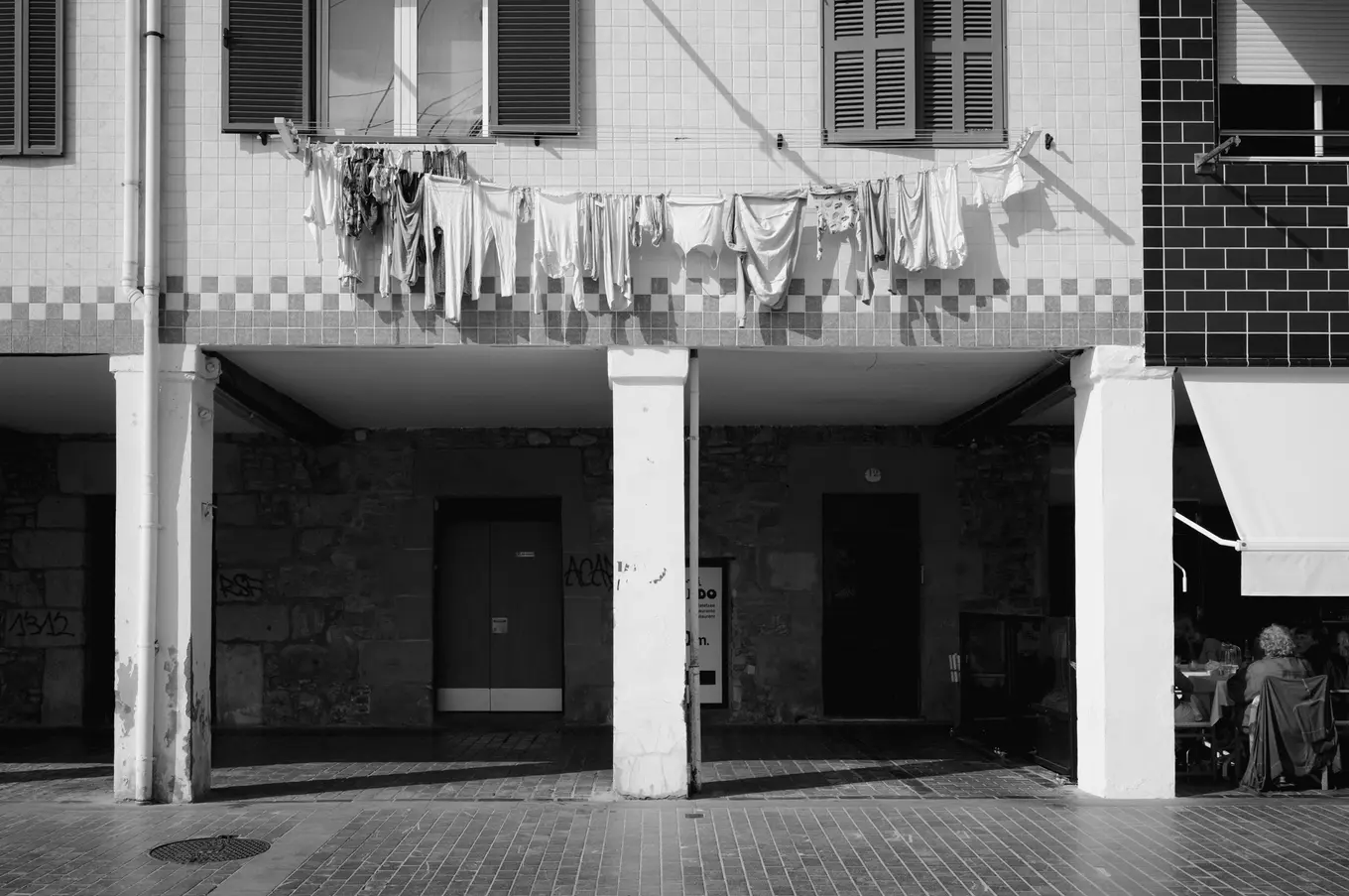 Washing on a line strung under the shuttered windows of a tiled house, arcades beneath