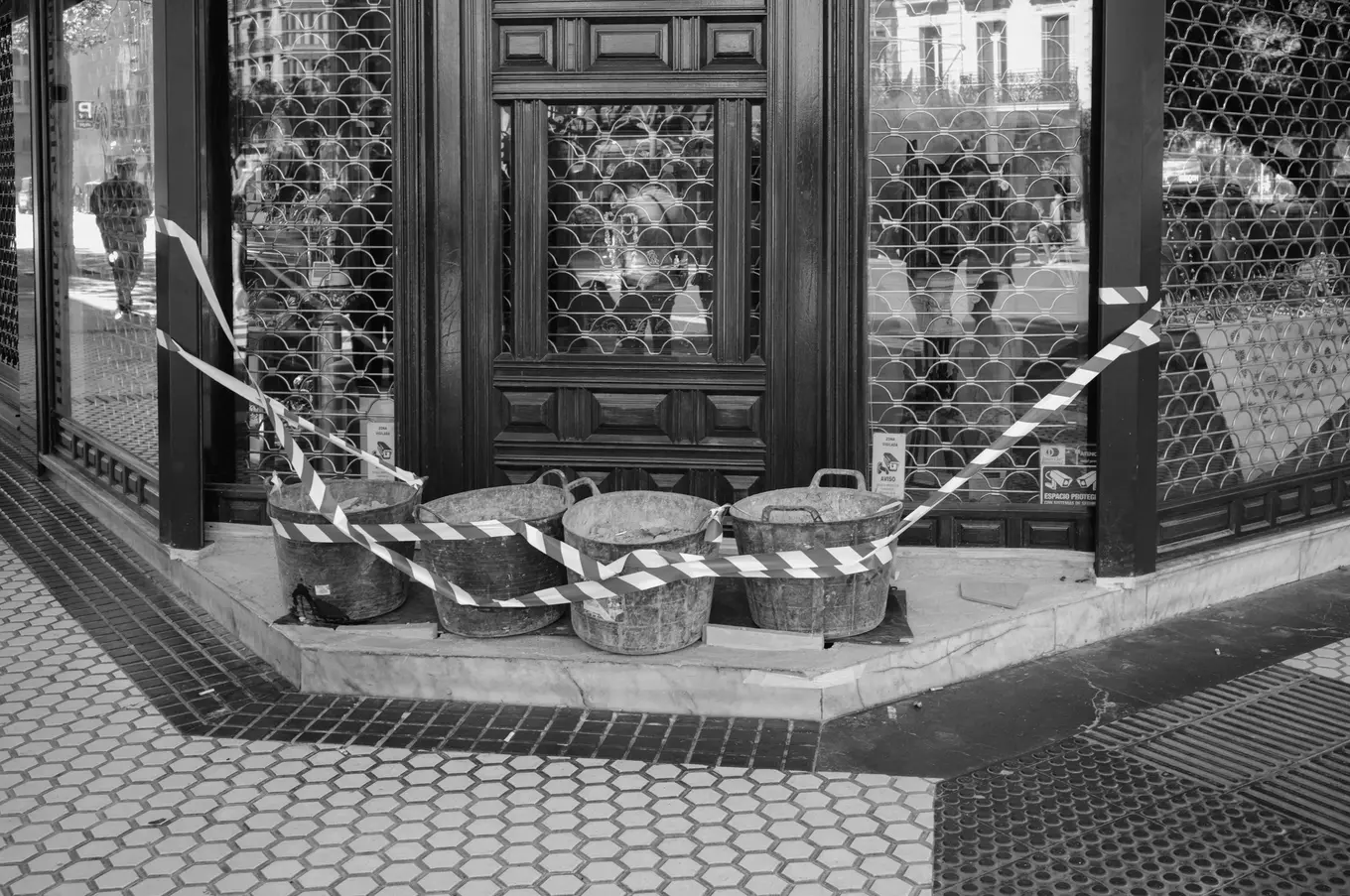 Four metal buckets taped off with hazard tape at the corner of a shuttered shopfront