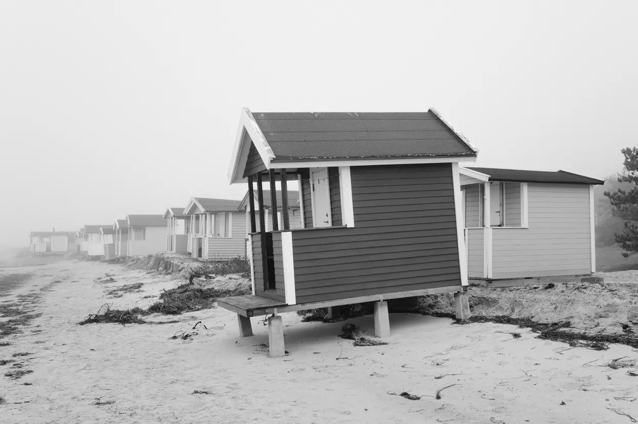 A dark-roofed hut on stilts, with the rest of the row receding into fog behind it
