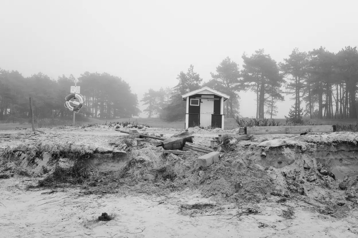 A small hut across a washed-out dune, a lifebuoy on a post to the left