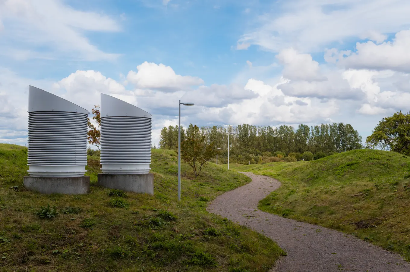 Two louvred vent stacks on concrete plinths, a path winding into the mounds behind them