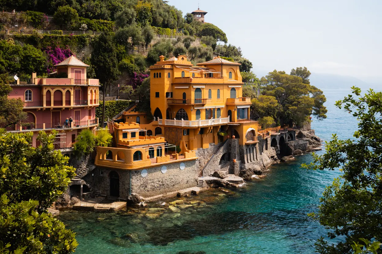 Ochre villas built out over clear green water, pines above them