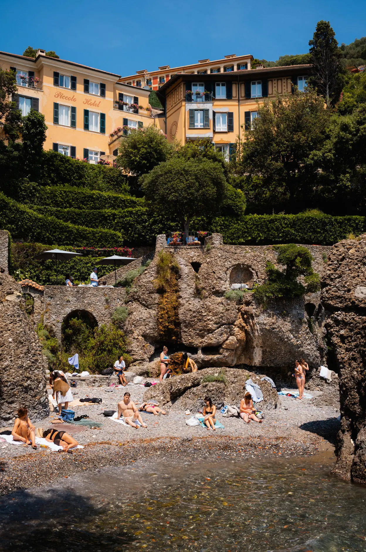 Sunbathers on a small pebble cove below a hotel and its terraced gardens