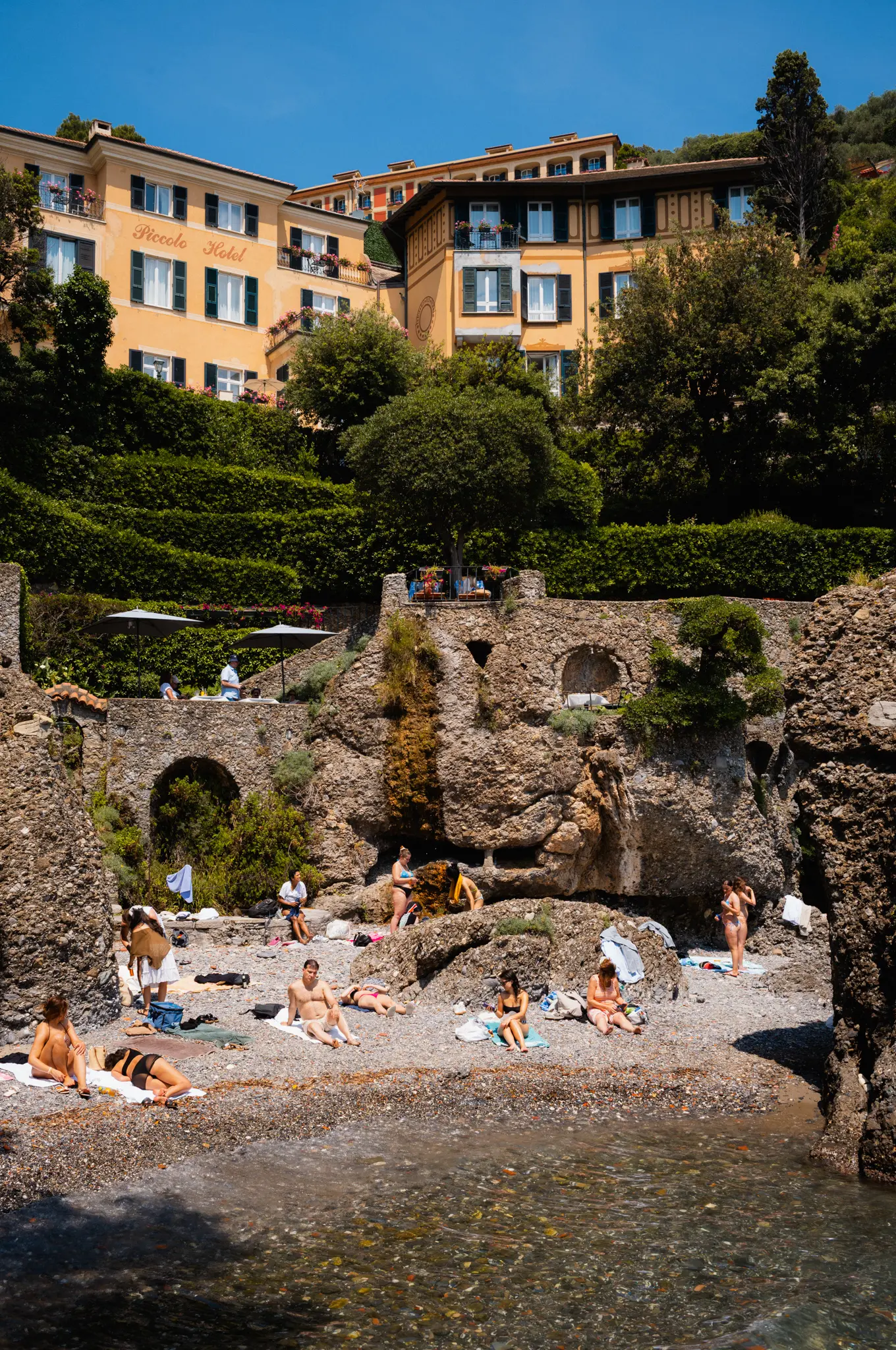 Sunbathers on a small pebble cove below a hotel and its terraced gardens