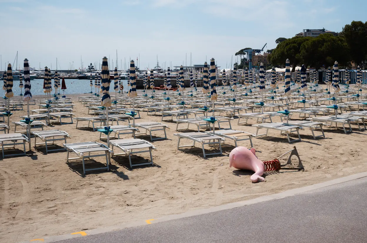 Rows of empty loungers and folded parasols on a beach, an inflatable left on the sand