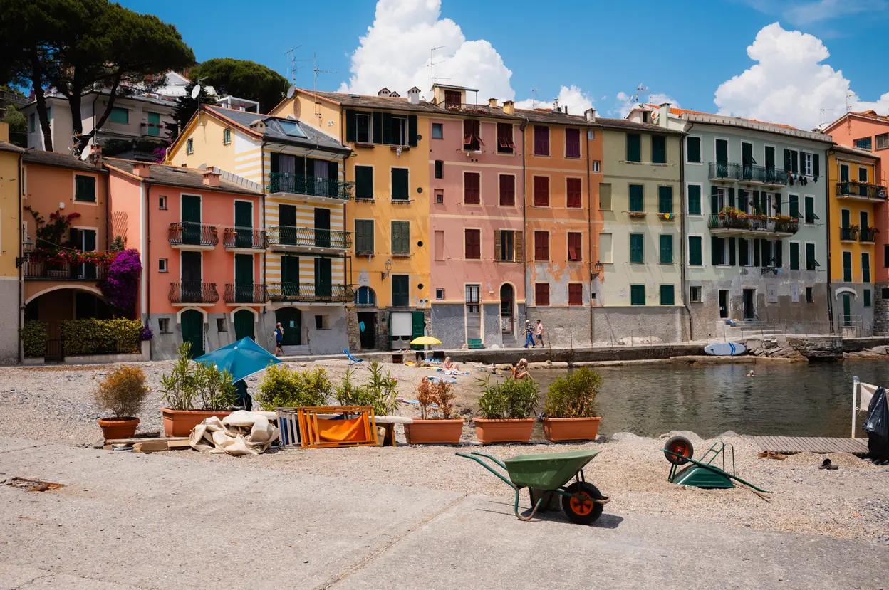 Pastel houses along a small harbor, a wheelbarrow standing on the sand