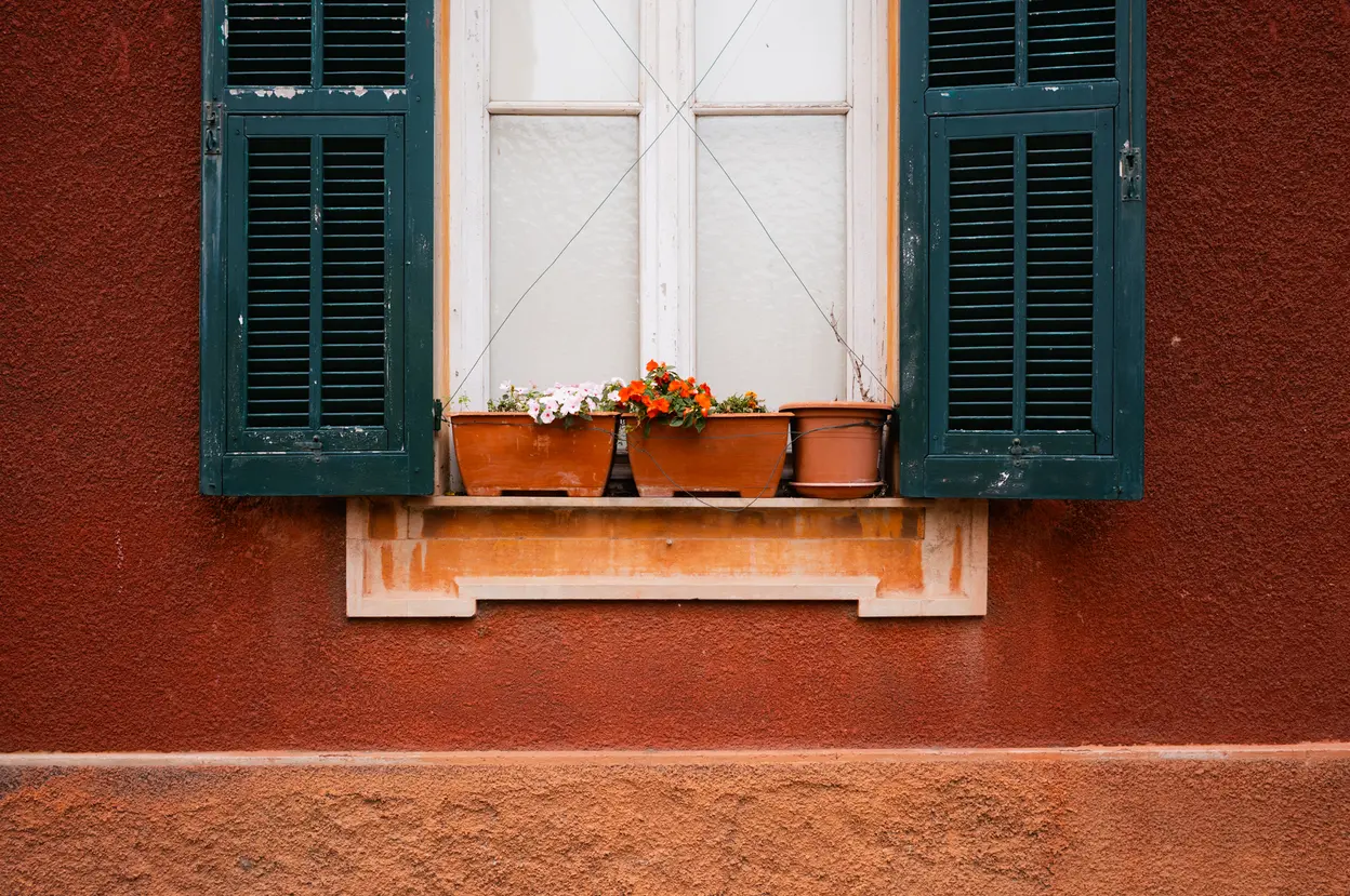 Green shutters and potted geraniums on a deep red wall