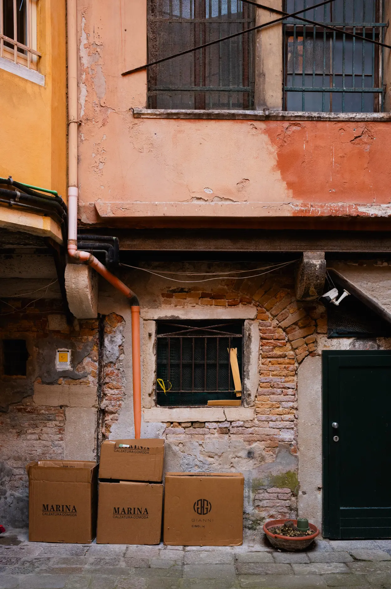 Cardboard boxes stacked under a window, an orange drainpipe running down the wall