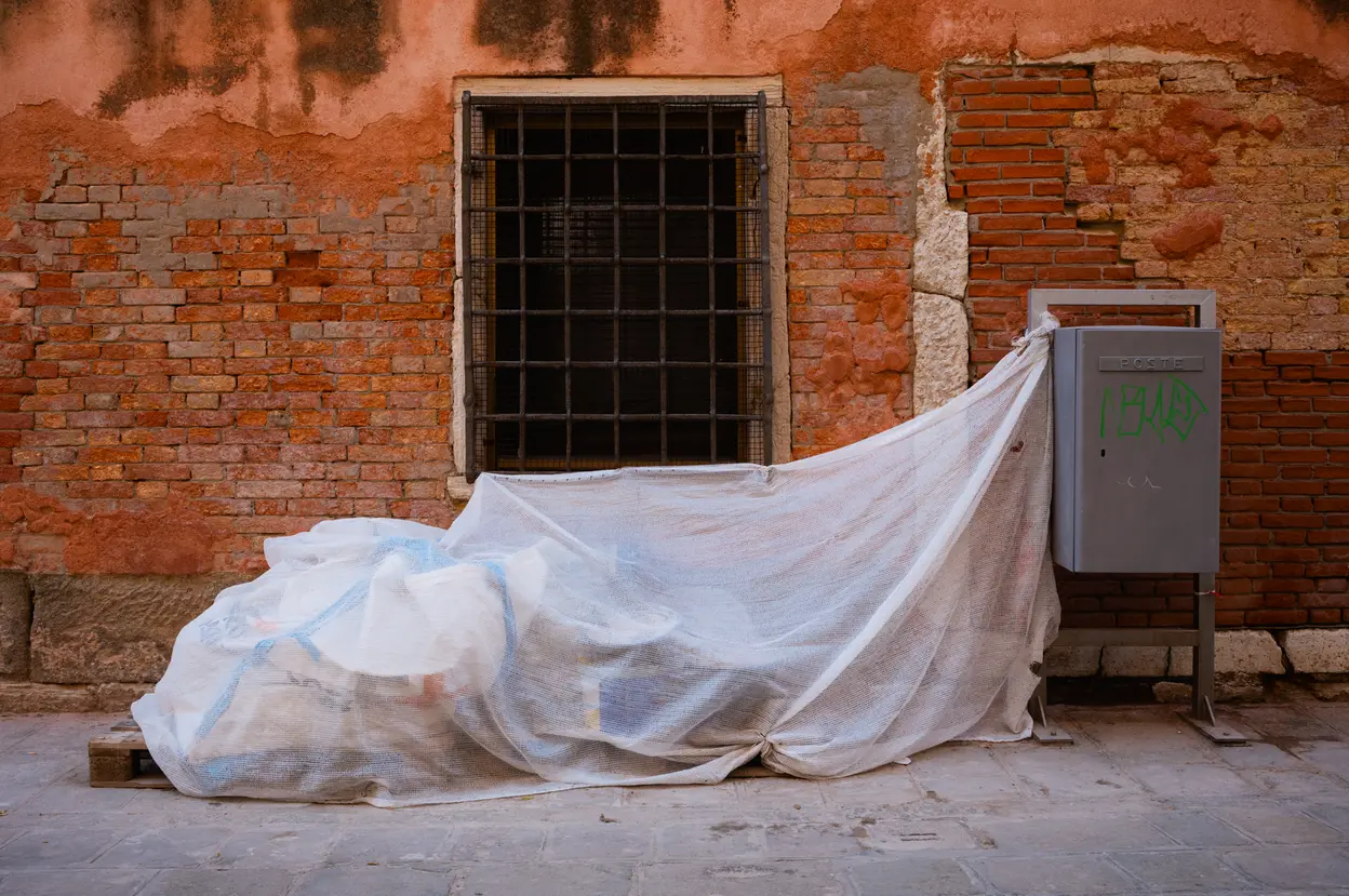 A sheet of plastic draped over something against a brick wall