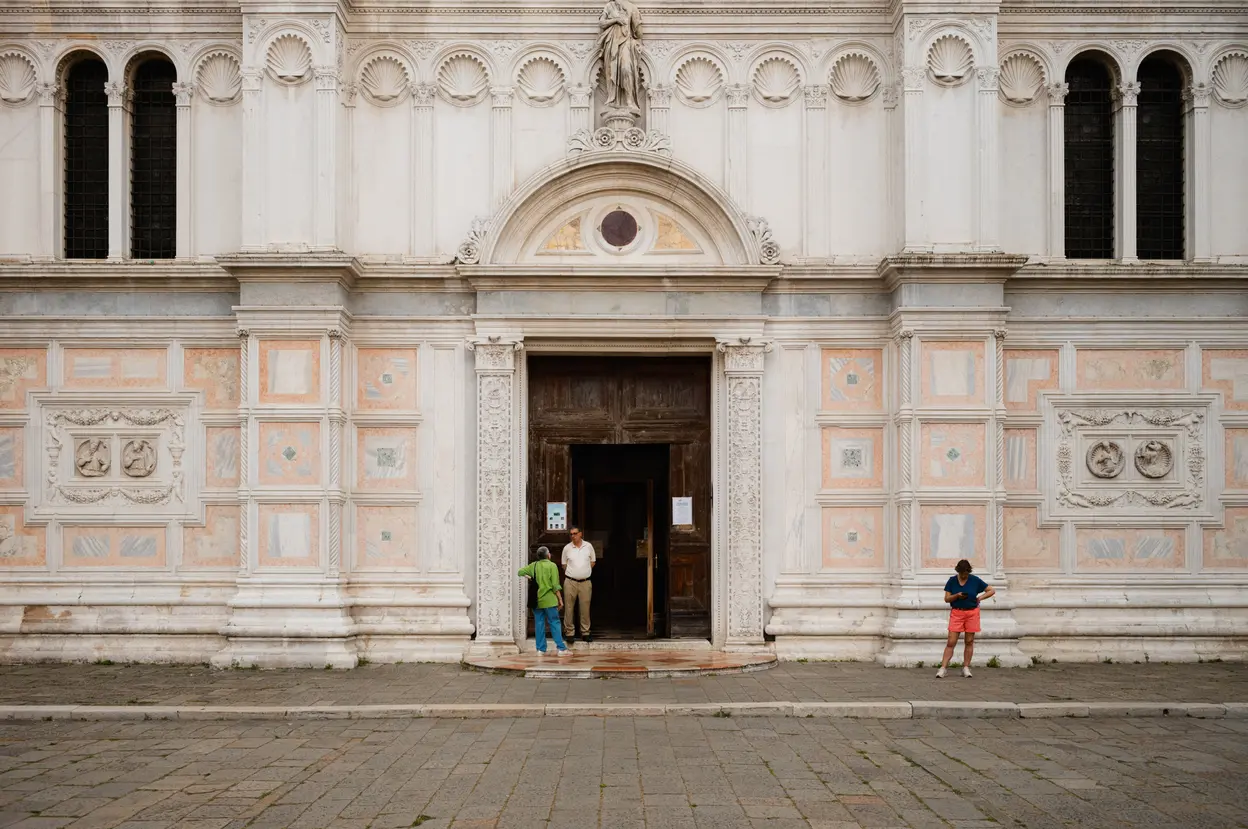 The marble front of a church, three people at its open door