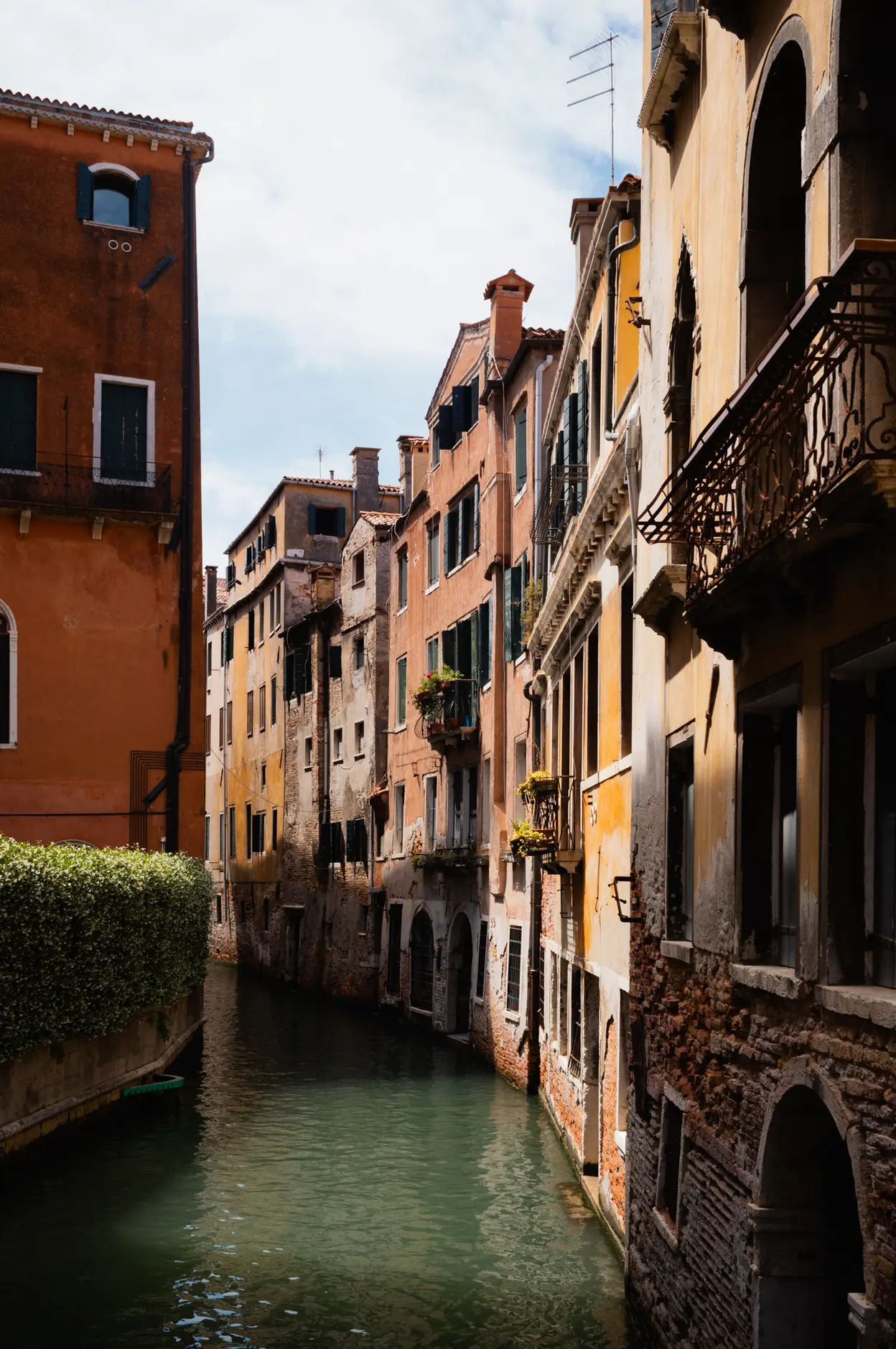 A narrow canal between leaning houses, shutters and window boxes above the water