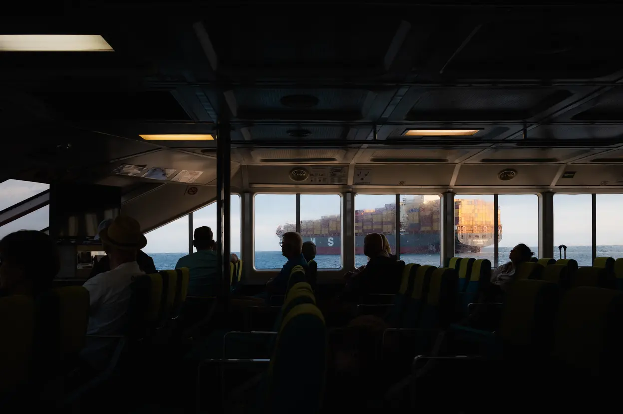 From inside a dark ferry cabin, a container ship passing across the windows